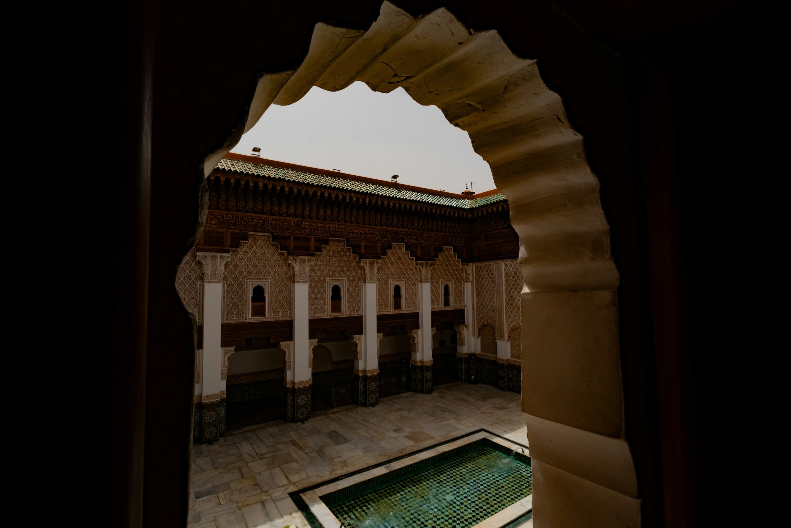 Arche sculptée ouvrant sur le bassin de zellige vert d’une cour de riad