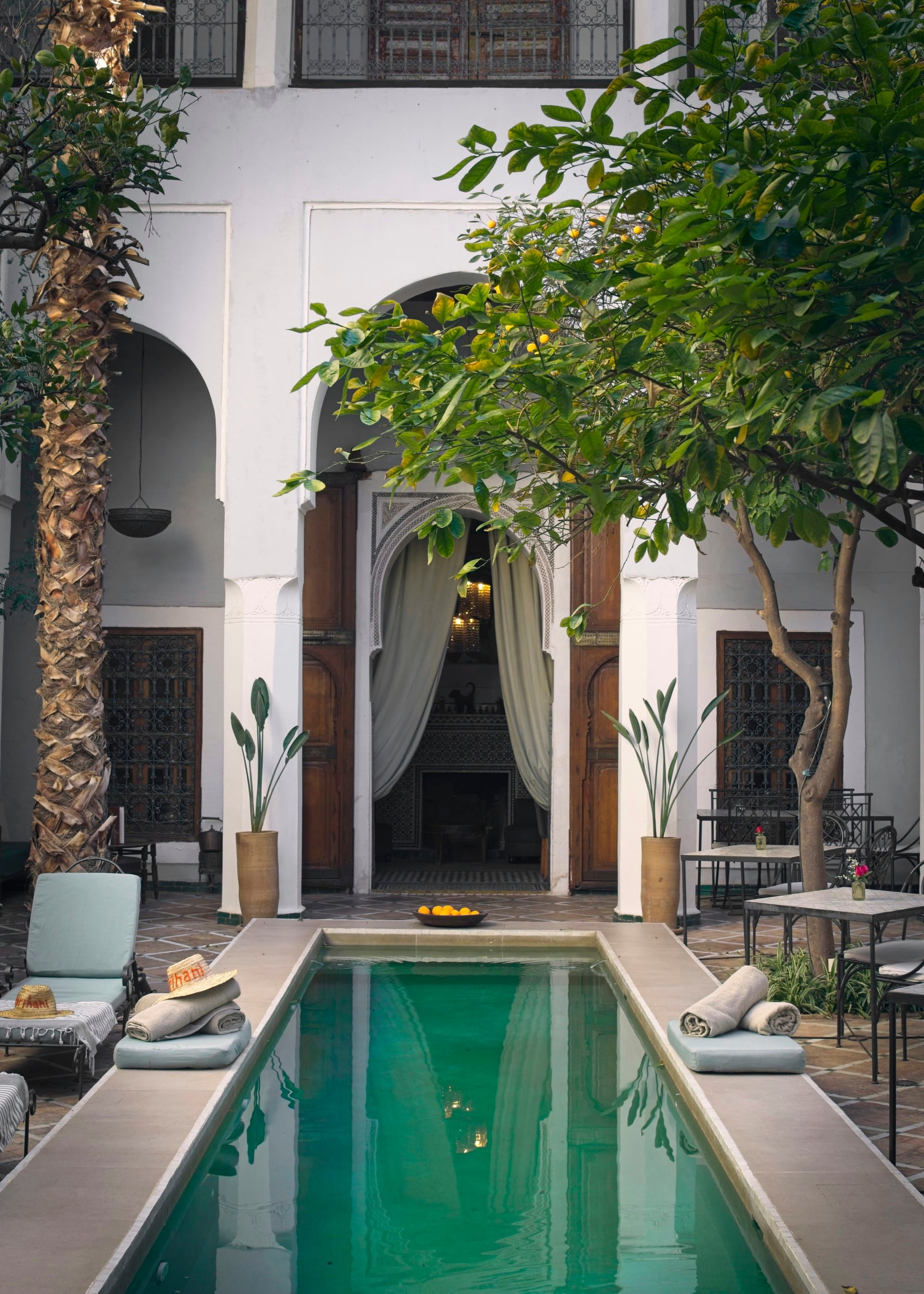 Cour de riad en plein jour, long bassin vert bordé d’oliviers en pot sous les arcades