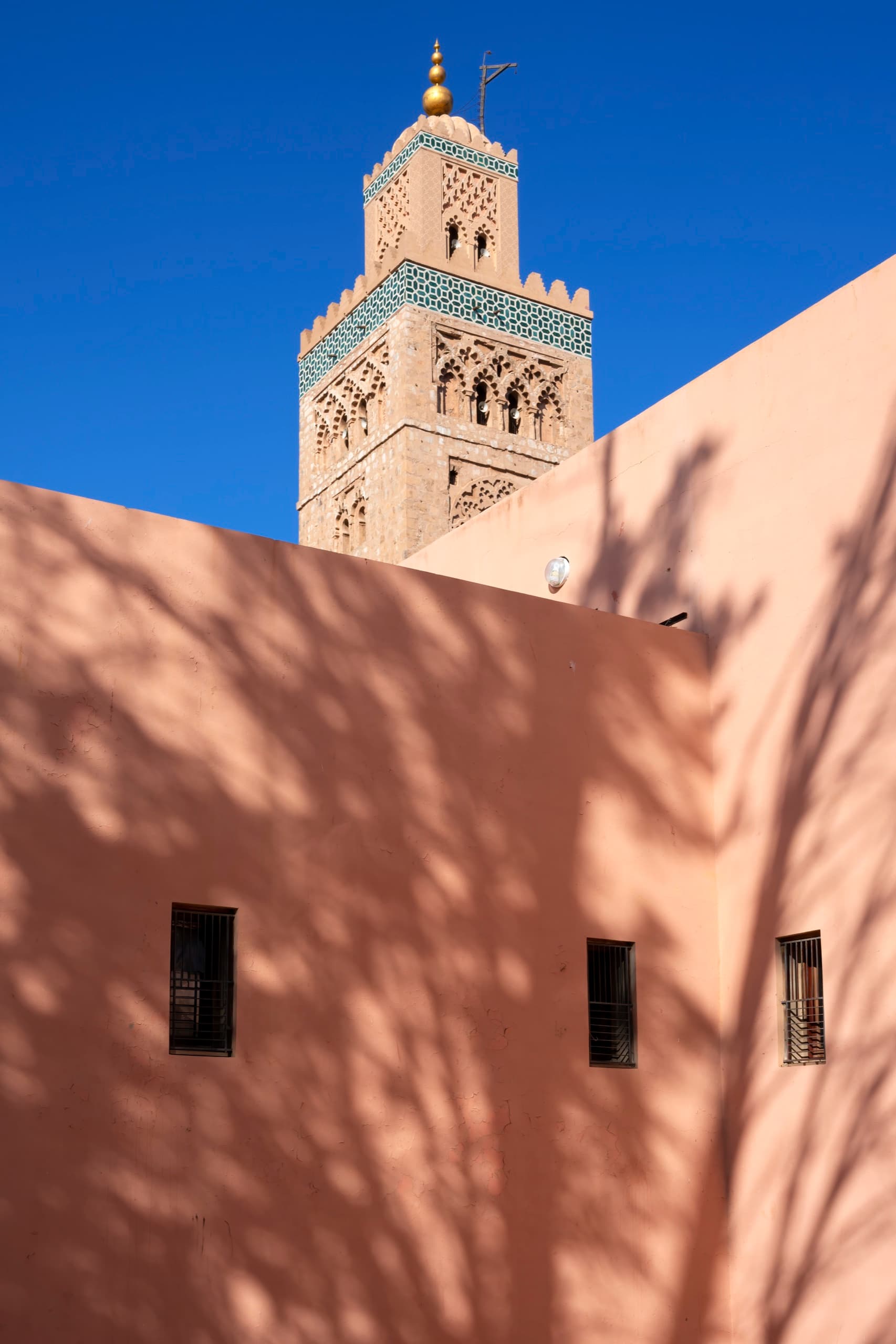 Minaret de la Koutoubia derrière un mur ocre marqué d’ombres de palmes, Marrakech