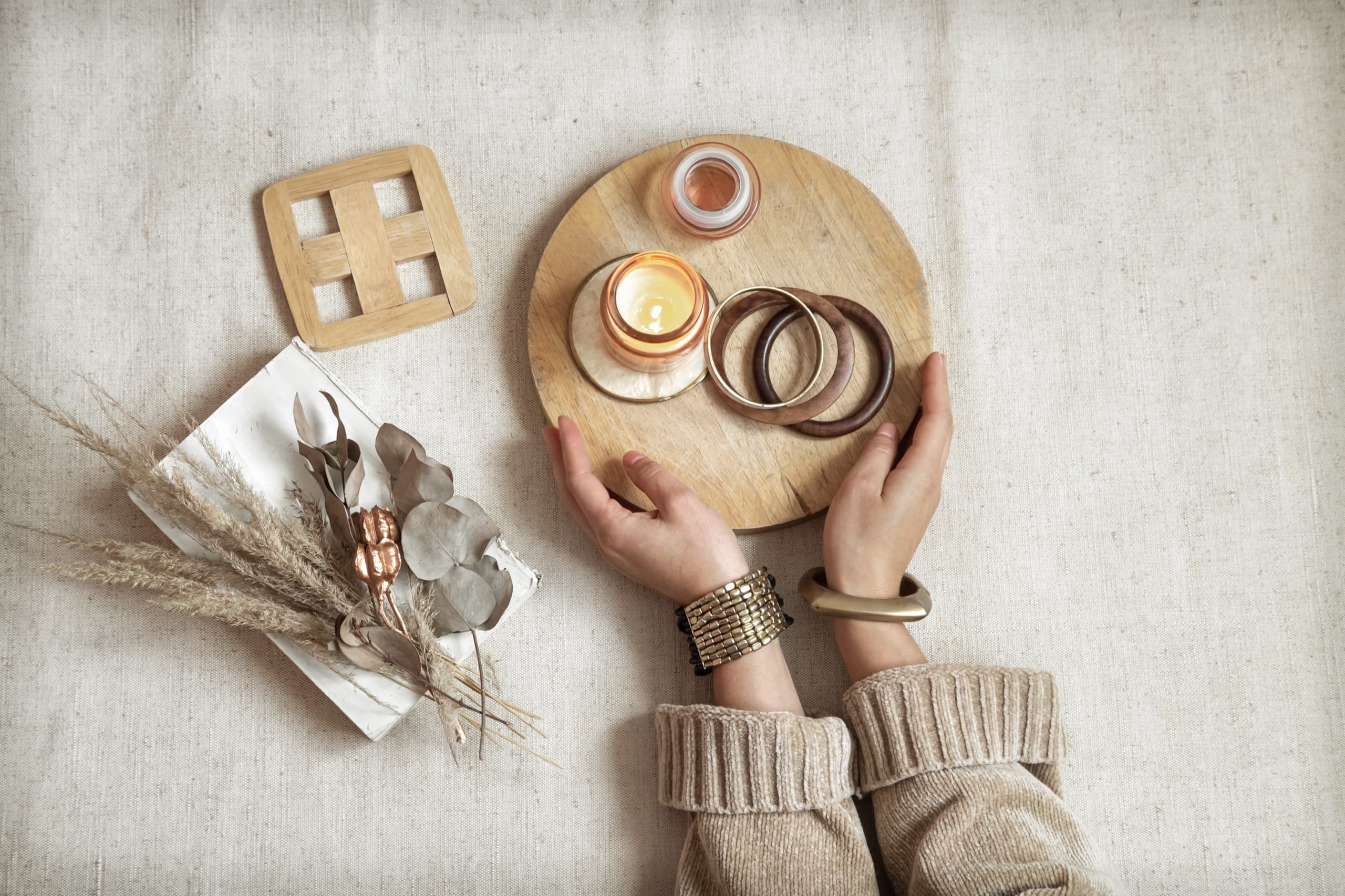 Deux mains disposant des objets et des fleurs séchées sur un plateau de bois, vue de dessus