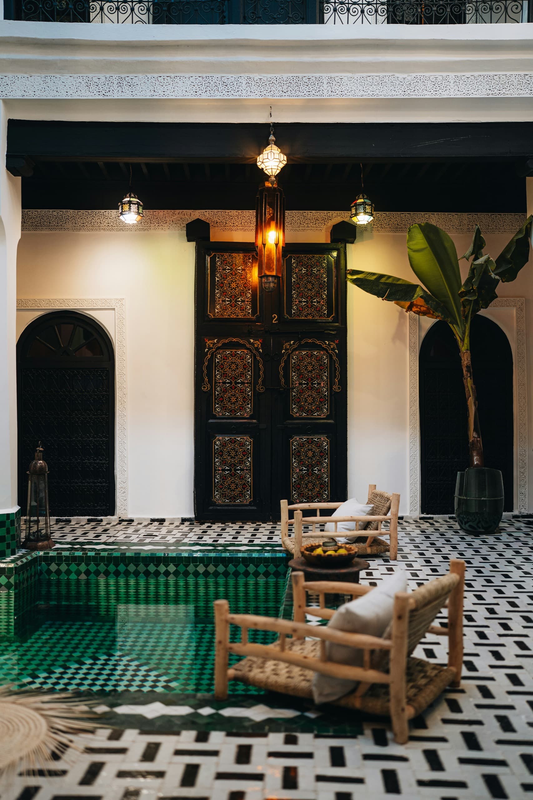Bassin de zellige vert dans une cour de riad, portes de bois sculpté et lanternes