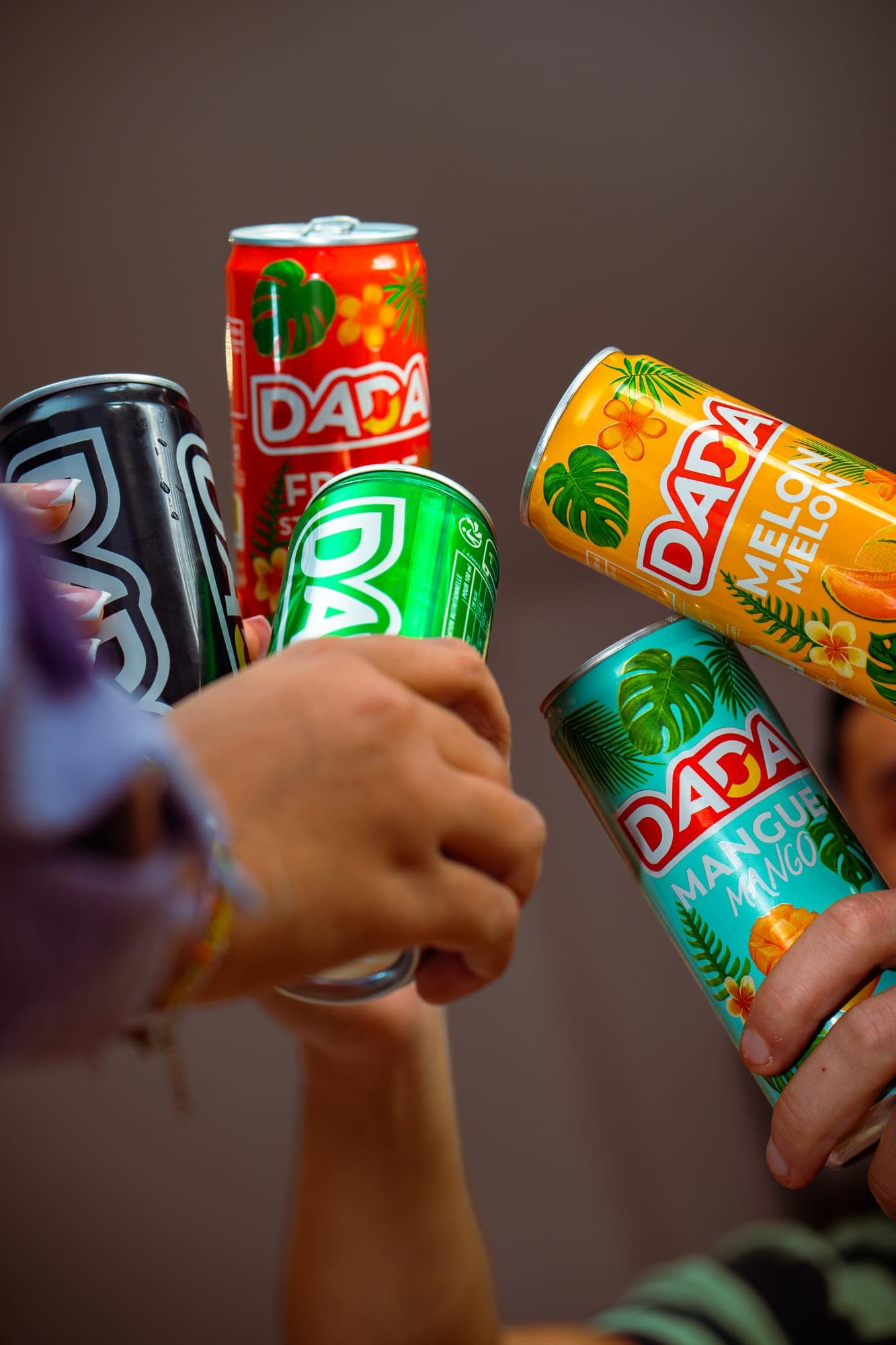 Cinq mains levant des canettes Dada de parfums différents pour trinquer