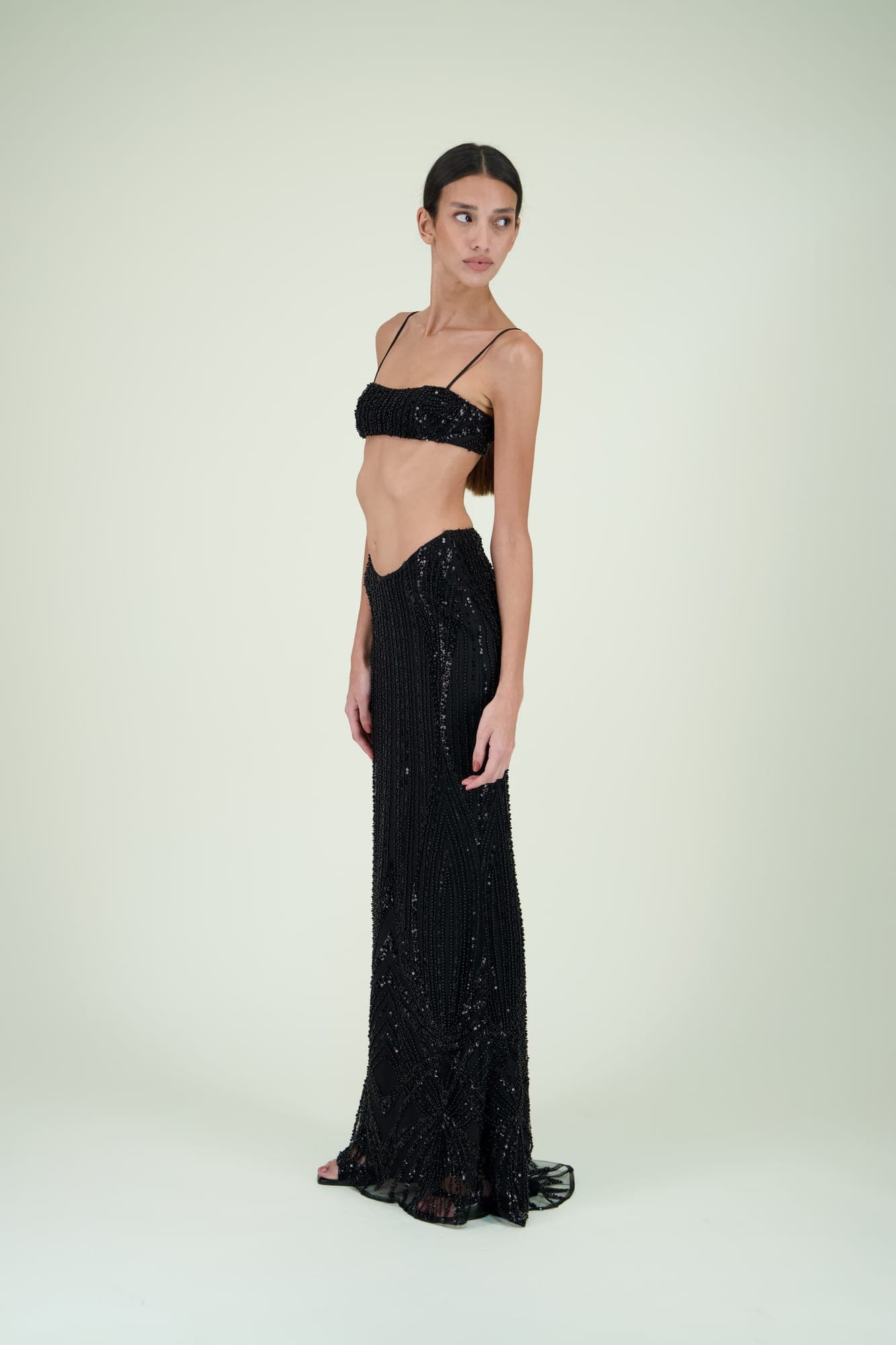 Mannequin en ensemble noir brodé, brassière et jupe longue à sequins, sur fond clair