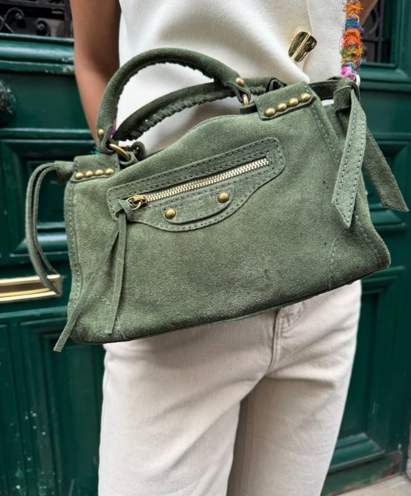 Sac à main en daim vert porté à l’épaule, devant une porte laquée verte